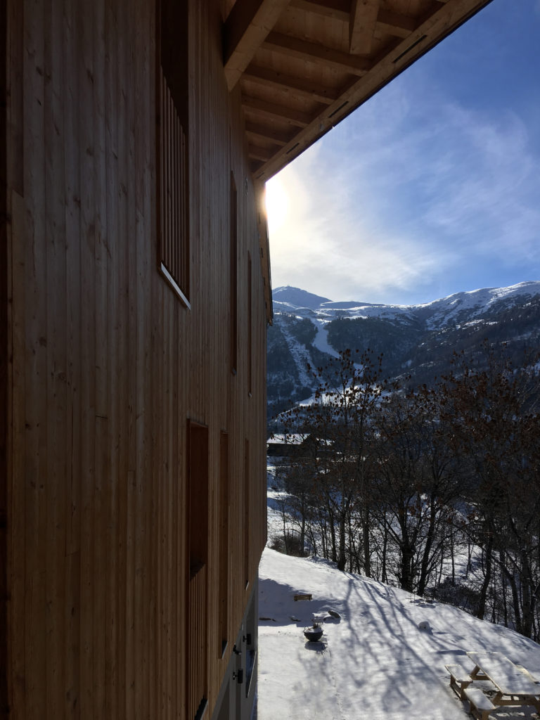 Gîte des Mille Thabor à Valmeinier : vue sur la partie du gîte et son bardage mélèze avec la station Galibier-Thabor en arrière-plan.